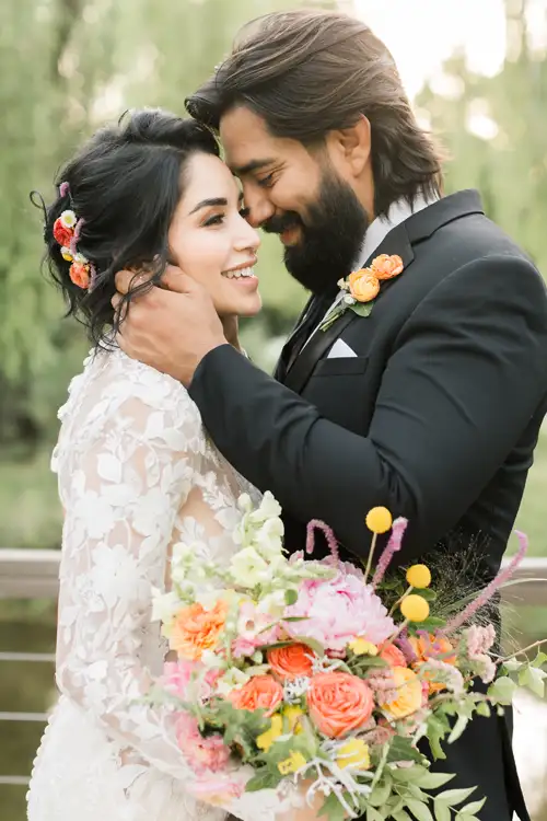 Couple on their wedding day sharing a kiss, the groom in a black suit holding the bride's face affectionatelly, bouquet in foreground